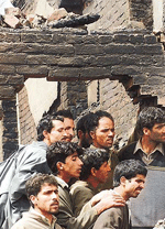 Villagers stand under the debris of a residential house gutted during a gunbattle at Dadoora village in Pulwama district, about 32 km south of Srinagar, on Sunday night.