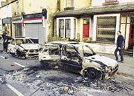 Cars are burned out, while shop windows are boarded up after being smashed in a night of riots in Burnley, England, on Monday. 
