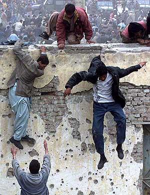 Fans jump over a stadium wall to get in.