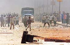 Rioters throw stones as a police vehicle passes by. 