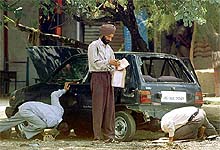 Members of a bomb disposal squad examine a damaged car