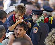  boy holds a flower as he rides on a mans shoulders during a memorial service at Ground Zero