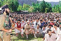 A securityman stands guard near a group of Kashmiri villagers 