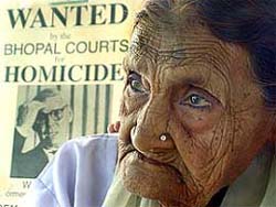 Mahmuda Bee, a 105-year-old survivor of the 1984 Bhopal gas disaster, sits in front of the poster showing Warren Anderson, former Chairman of Union Carbide