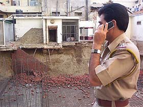 A policeman surveys the wall that caved in and killed two labourers
