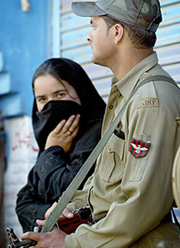 A Kashmiri woman stands besides a securityman during a National Conference rally