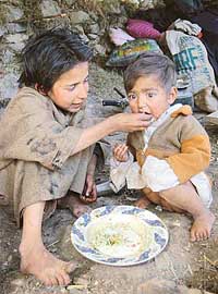 A girl tries to feed her younger sister amidst the ruins of their house which was destroyed in the recent earthquake in Kamlkote, about 130 km north of Srinagar, on Friday.
