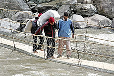 A Pakistani porter (right) helps Indian porters carry relief material on a footbridge connecting the two Kashmirs at Chiliana, in Neelum valley on Saturday.