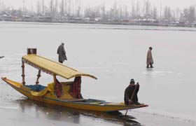 Two Kashmiri youths walk on the frozen surface of the Dal Lake, while a Kashmiri boatman guides his shikara through a narrow channel of water in Srinagar