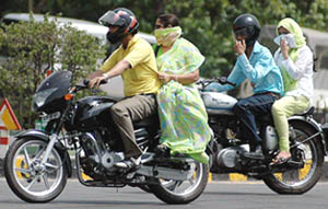 Pillion riders cover their faces to protect themselves from the heat on a hot summer afternoon in New Delhi on Sunday. A blistering heat wave swept most places in North India.