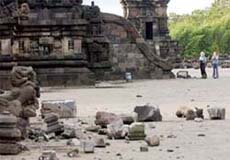 Tourists walk through a destroyed Hindu temple with pieces of columns lying on the ground in Prambanan, Yogyakarta, Indonesia