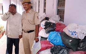 Vinod Sharma covers his face as he stands next to the seized sacks of the banned drug mandrax at a police station in New Delhi