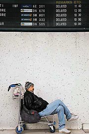 A passenger rests under the message board at the domestic airport as flights are delayed due to fog in New Delhi on Tuesday.