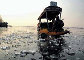 A man paddles his Shikara on the frozen water of famous Dal Lake in Srinagar