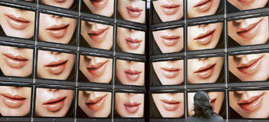 A woman looks at video screens displaying a cosmetic commercial