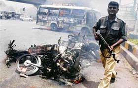 A Pakistan policeman passes by burning vehicles during clashes, which erupted between the government and opposition supporters in Karachi
