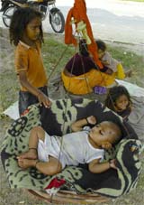 This little girl takes care of her young sibling while her mother is busy with other chores.