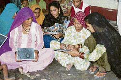 Raj Pati shows the slate after writing her name on it while “akshar sainik” Kamlesh gives writing tips to other rural women at a literacy class in Baijalpur village in Fatehabad district.