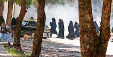 A masked Pakistani radical student (left) of Lal Masjid takes cover behind a tree as veiled students run to avoid tear gas during an exchange of fire between radical students and paramilitary soldiers outside the mosque in Islamabad on Tuesday.