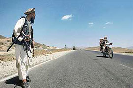 An Afghan policeman wearing traditional clothing watches as a motorcyclist approaches a checkpoint on the edge of Ghazni, on Friday.