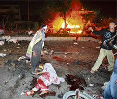 People help an injured as bodies lie at the bomb explosion site in Karachi on Thursday as Bhutto's homecoming parade was hit by two apparent suicide attackers who killed at least 80 persons.