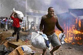 Looters with stolen goods run past burning shacks at the Kibera slum in Nairobi