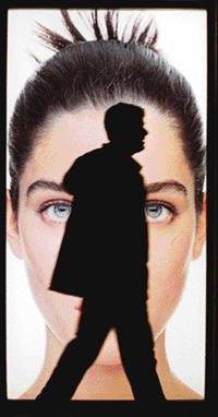 A man’s silhouette partially eclipses a model’s face as he walks past a billboard.