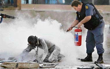 A policeman try to save a man who was set alight by a mob during clashes believed to be linked to recent anti-foreigner violence in Reiger Park informal settlement east of Johannesburg