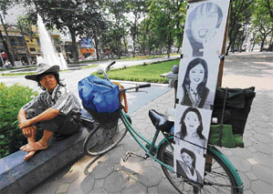 A street artist sits next to his bicycle showing portraits of some local celebrities as he waits for customers at a public park in downtown Hanoi, Vietnam. The artist charges 30,000 dongs (1.9 USD) for a 15-minute portrait session.