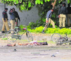 The body of one of the two suspected suicide bombers lies on a road as policemen secure the area of the blasts at Wah, near Islamabad, on Thursday. The attackers blew themselves up almost simultaneously outside two gates of the sprawling factory complex. It is one of the country's most sensitive installations.
