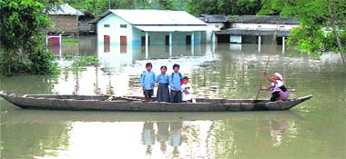 Schoolchildren use a country-made boat through a flooded street at Majuli in Jorhat district of Assam