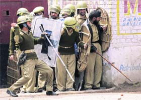 A policeman throws back stones towards protesters as other policemen take cover behind a wall during a protest in Srinagar