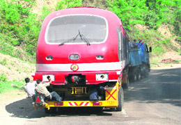 Two maintenance workers hang on to the rear of the railway coaches being rolled on the National Highway from Jammu to Badgam.