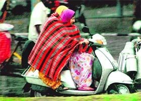 Two girls share a shawl as they breeze by on a scooter