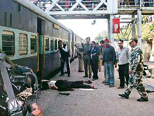 People stand near the body of a victim after a bomb blast at the Diphu railway station in Karbi Anglong district of Assam on Tuesday. 