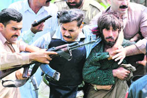 Pakistani security officials arrest a suspected militant (right) near the site of a police training centre in Lahore on Monday.
