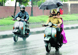 Rain fails to dampen the spirit of this couple who ride their scooter under the cover of an umbrella.