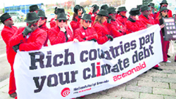 Members of envi- ronmental activist group Act!onaid, dressed asclimate debt agents, hold up a banner out- side the congress centre at the UN Climate Change Conference in Copenhagen