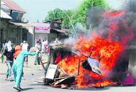 A woman hurls stones at a burning government vehicle after protesters set it on fire during the funeral procession of Tanveer Ahmad at Pampore on the outskirts of Srinagar