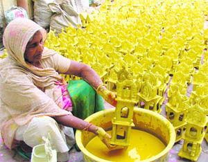 A woman colours miniature huts to be put on sale on Diwali, in Ludhiana on Saturday.