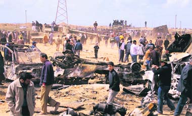 Trail of destruction: Onlookers gather at a site, about 35 km west of Benghazi, bombed by coalition forces on Monday. Reports said Muammar Gaddafis forces had retreated 100 km from Benghazi