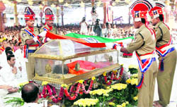 Policemen drape the National Flag over the casket of Sri Sathya Sai Baba ahead of his burial inside 