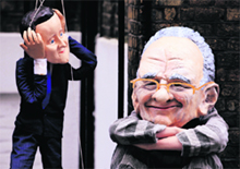 A protester wearing a caricature giant head depicting Rupert Murdoch sits next to a puppet of Britain's PM David Cameron outside Murdochs apartment in London 