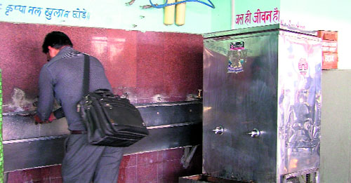 A man drinks water from an ordinary tap while a water cooler lies non-functional at the bus stand in Ludhiana.