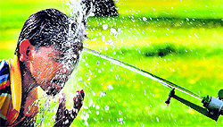 A boy enjoys a splash of water from a sprinkler in Chandigarh