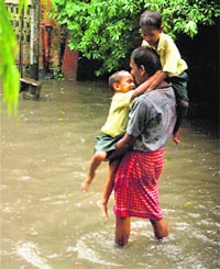 A man, carrying two children, wades through a waterlogged road after heavy rains in Kolkata.