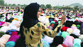 A girl takes a picture of devotees offering prayers at an Eidgah in Srinagar.