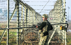 A BSF jawan patrols the fenced border with Pakistan in Suchetgarh, southwest of Jammu, on Friday.