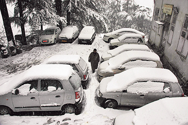 A man walks past snow covered vehicles in Shimla on Wednesday.
