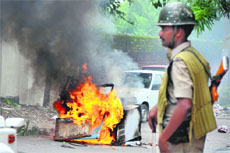 A security man stands guard after a furniture shop was set on fire in Subash Nagar area of old Jammu city on Sunday. 